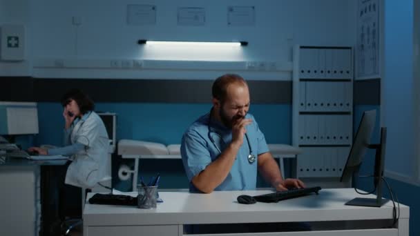 精疲力竭的医生助理一边在电脑上打字 一边在病人药物治疗中工作了好几个小时 疲惫不堪 医院办公室的临床工作人员检查报告 — 图库视频影像