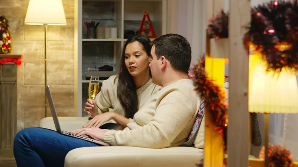 Romantic couple relaxing on couch and browsing on their phones for christmas gifts. Holiday xmas online shopping with credit card via internet, web, searching for season sales. Surprise discount shop
