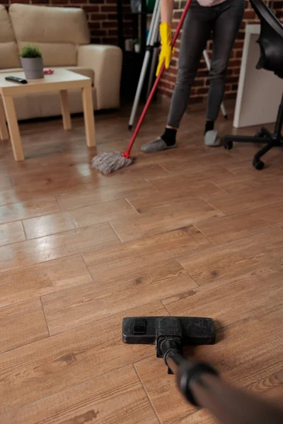 Unrecognizable people concentrating on cleaning house, using vacuum cleaner and dusting tile floor. Doing household chores, cleaning and tidying living room in urban apartment.