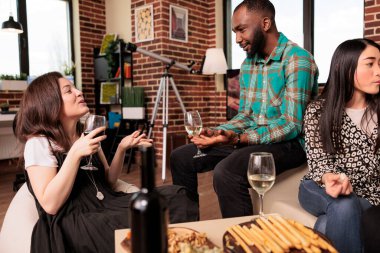 İş ziyafetinde, Afro-Amerikan erkek, beyaz kadın, ortak çiftler arasında mutlu bir sohbet. Genç, etnik çeşitlilikte genç bir çift şarap içiyor, birbiriyle konuşuyor, atıştırmalıkların tadını çıkarıyor..