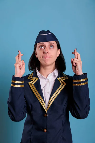 Portrait of prayer stewardess crossing fingers, looking up, praying for luck before flying. Superstitious flight attendant getting lucky, pleading for success with hopeful facial expression