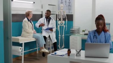 General practitioner consulting elderly woman in cabinet, talking about disease diagnosis and treatment support. Male doctor giving medical advice at checkup visit with senior patient.