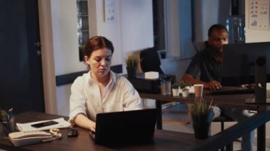 Ofis çalışanı geceleri dizüstü bilgisayarda çalışıp kol saatini kontrol ediyor, saate bakıyor ve mesai sonrası işte oluyor. Web belgeleri planlayan ve e-posta gönderen bir kadın. El kamerasıyla..
