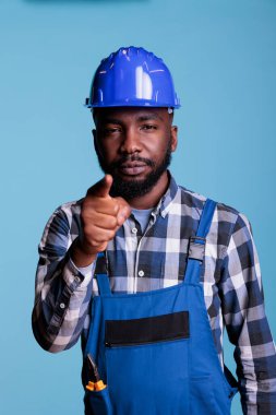 Afrikalı bir adamın mavi arka planda duran işaret parmağıyla çektiği portre. Yönünü belirten ve seni seçmeye karar veren inşaat işçisi, stüdyo çekimi..