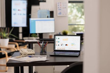 Portatif bilgisayar ekranı olan, kazanç istatistiklerini yansıtan boş bir finans şirketinin içinde. Yatırım işyeri. Arka planda kimse yok. Dev ekran grafikleri gösteriyor..