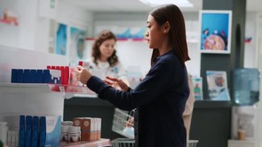 Eczane raflarındaki kardiyoloji ilaç kutusuna bakan Asyalı bir müşteri, ilaç ve sağlık malzemeleri alıyor. İlaç ve ilaç almak için ilaç broşürlerini kontrol eden kişi. El kamerasıyla..