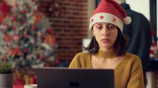 女雇员分析笔记本电脑上的研究数据 在圣诞节前夕戴着圣诞礼帽 在庆祝冬季活动之前 在电脑上计划报告 三脚架射击 — 图库照片