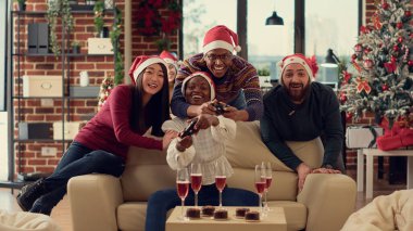 Neşeli insanlar kış tatili partisinde çevrimiçi video oyunlarıyla eğleniyorlar, Noel arifesini ofiste kutluyorlar ve konsolda oynuyorlar. Xmas festivalinde yarışmayla eğleniyorum. Üçayak atışı.