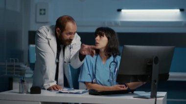 Pratisyen ve hemşire, hastane ofisinde saatlerce çalışırken hasta hastalıkları uzmanlığını inceleyen bilgisayarın tıbbi raporunu kontrol ediyorlar. İlaç hizmeti ve konsept