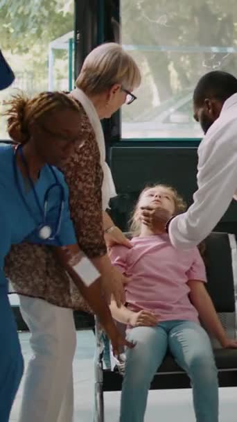 垂直ビデオ めまいの病気の子供と一緒に来るシニア男性と女性は 医療からの緊急検査を求める相談に参加します 病院の待合室で頭の光を感じる病気の女の子 — ストック動画