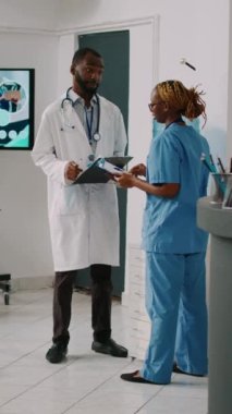 Dikey video: Afro-Amerikan uzman ekibi hastane resepsiyon lobisindeki randevular ve hastalık tedavileri hakkında konuşuyor. Sağlık merkezinde çalışan hemşire ve hekim tıp hakkında konuşuyor.