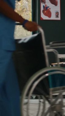 Dikey video: Genç bir adam ve kadın yaşlı bir yetişkinin check-up muayenesine katılmasına yardım ediyor, kalp sorunu olan hasta hastayı tıbbi tesise getiriyor. Mide ekşimesi olan birini muayene eden doktor..