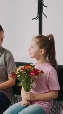 Dikey video: Anne ve küçük çocuk tıbbi randevudan önce bekleme odasında oturuyor, elinde bir buket çiçek tutan kız. Genç bir çocuk ve kadın lobide doktorla birlikte muayeneye katılmak için bekliyorlar..