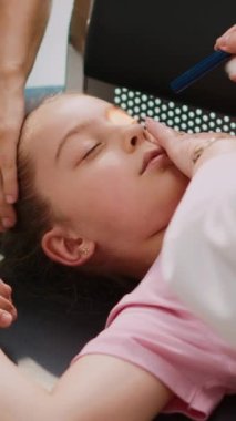 Dikey video: küçük bir çocuk hastane bekleme salonunda bayılıyor, yaşlı bir doktor el feneriyle acil durum danışmanlığı yapıyor. Hasta ve baygın bir kızı destekleyen endişeli bir kadın. El kamerasıyla.