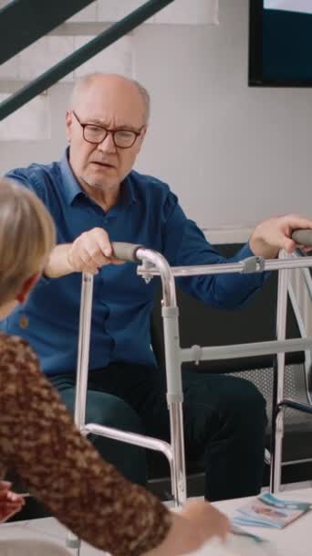 垂直ビデオ 病院の受付ロビーで待機している高齢者は 専門家と一緒に視察試験に出席します 保健所の待合室に座っている高齢者 医療施設での検査 — ストック動画