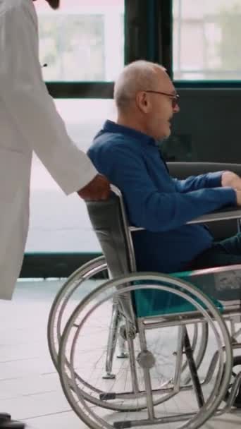 垂直录像 医生带着坐着轮椅的老人与妇女和儿童交谈 保持健康 并开始带着步行架走路 长者病人在健康中心康复 — 图库视频影像