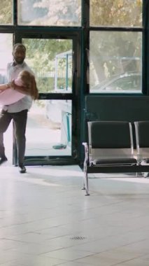 Dikey video: Baba, uzman, endişeli ebeveynlerden yardım almak için sağlık merkezinde bilinçsiz bir çocuk taşıyor ve doktorla acil konsültasyon için bekliyor. Hasta kıza tıbbi danışmanlık