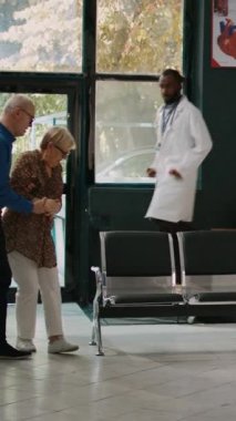 Dikey video: Erkek doktor kalp basıncı olan yaşlı kadına danışıyor, bekleme odasında mide ekşimesi yaşıyor. Kalp sorunları ve kardiyovasküler hastalığı olan hastaya danışmanlık yapılıyor
