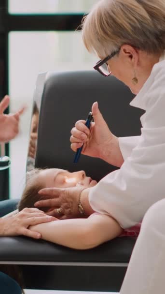 垂直ビデオ 小児病院の待合室で気絶 高齢者の医師は懐中電灯で緊急相談を行う 小さい子供が病気で意識不明であることを支える心配の母 手持ち — ストック動画
