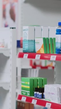 Dikey video: Genç bir adam eczane raflarından ilaç alıyor, reçeteli tedavi için ilaç sepetine koyuyor. Asyalı istemci vitamin ve takviye kutularını işaretliyor