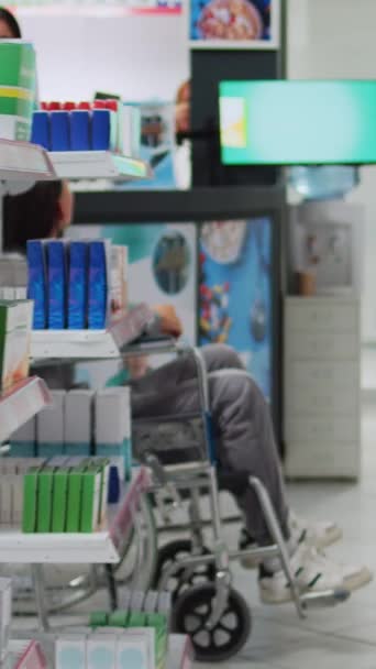 垂直录像 残疾患者和社会工作者在药房获得医疗用品 购买保健产品 接受药物治疗的轮椅顾客 药剂师 — 图库视频影像