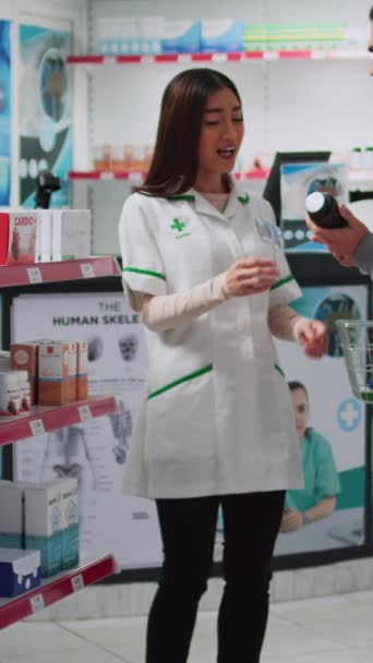 垂直ビデオ 薬のボトルを顧客に示し 処方治療と棚からの医療用品を提供する医療コンサルタント 医薬品についてお客様と話すスペシャリスト — ストック動画