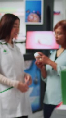 Dikey video: Eczanede kardiyoloji kardiyolog kutusunu analiz eden kadınlar, eczacının müşteriye ilaç ve malzeme vermesi. Kadın ve eczane çalışanı sağlık malzemeleri paketlerine bakıyor..