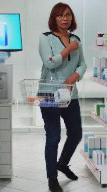 Dikey video: Kadın müşteri ilaç kutularını sepete koyuyor, reçeteli tedavi için ilaç paketlerine bakıyor. Kadın takviye ve vitaminleri kontrol ediyor, eczacılık sağlık hizmetleri...
