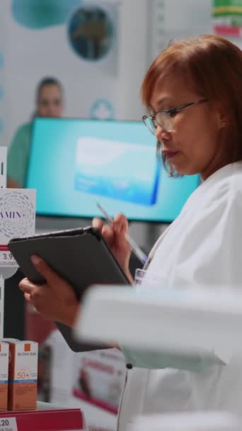 垂直ビデオ アジアの従業員は若い男性に薬の箱を与え 顧客を助け 消耗品在庫に取り組んでいます 薬剤師は薬のパッケージを分析し 顧客に薬を示す — ストック動画