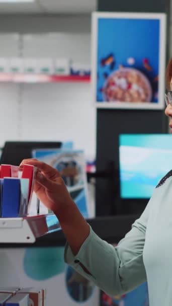 垂直ビデオ 医薬品を見ている女性のバイヤーは 棚に薬のパッケージを分析し 薬を見つけるために 薬やサプリメントを探す女薬局だ 手持ち撮影 — ストック動画