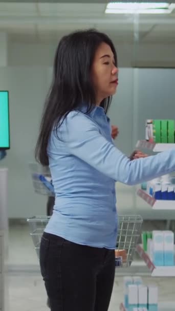 垂直ビデオ ドラッグストアでビタミンや医薬品を探している女性の顧客を助けるために若い薬剤師の提供 治療や薬箱を見つけるために女性を助ける医療専門家 — ストック動画