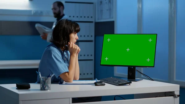 診察予約時に夜遅くに緑色の画面が表示されたコンピュータを見て机の上に立つ医療補助者 病院で患者の専門知識を入力する医師看護師 — ストック写真