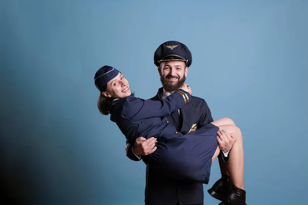 微笑的飞行员手持飞行服务人员的武器肖像 穿着专业制服的机组人员看着相机 快乐的飞行员和空姐浪漫夫妇演播室中镜头 — 图库照片