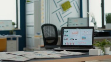 Empty startup office with laptop showing business mangement software on display showing moving charts and statistics on desk. Interior of marketing department with portable computer with erp.