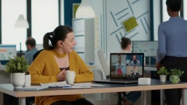 Startup office employee using laptop in video conference with clients and manager talking about marketing strategy. Casual business woman in group call discussing with remote coworkers about charts.