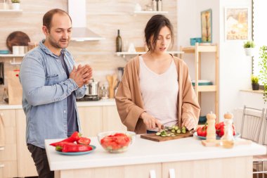 Mutfakta salatalık kesen bir kadın kocasıyla konuşurken sağlıklı salata yiyor. Mutlu aşıklar, neşeli ve kaygısız çiftler yemek hazırlamak için birbirlerine yardım ediyorlar.