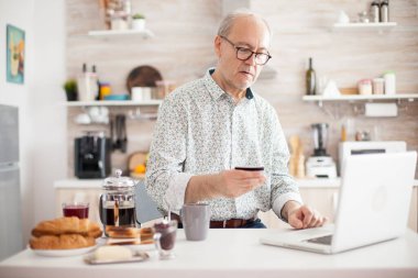 Son sınıf öğrencisi sabah mutfağından online alışveriş yapıyor. Emekli, internetten kredi kartı ve dizüstü bilgisayardan başvuru ile ödeme yapıyor. Emekli yaşlı kişi internet ödemeli ev bankası satın alımı kullanıyor