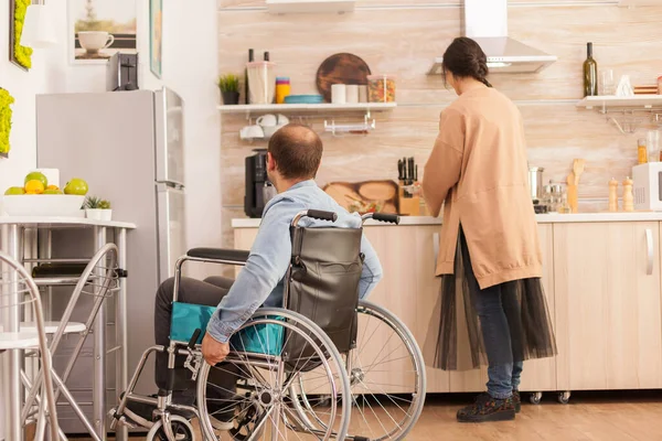 轮椅上有行走障碍的男人看着妻子是怎样做饭的 事故后有行走残疾的瘫痪残疾人融入社会 — 图库照片