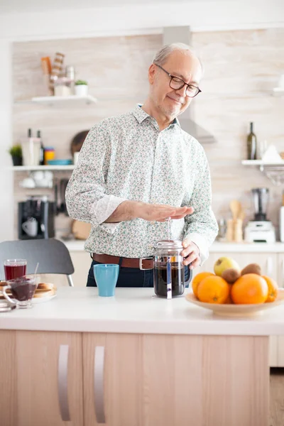 Senior man making coffee using french press during breakfast in kitchen. Elderly person in the morning enjoying fresh brown cafe espresso cup caffeine from vintage mug, filter relax refreshment