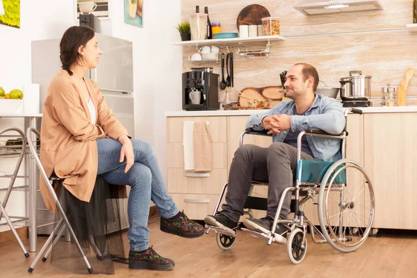 坐在轮椅上的残疾人看着厨房里有爱心的妻子 事故后有行走残疾的瘫痪残疾人融入社会 — 图库照片