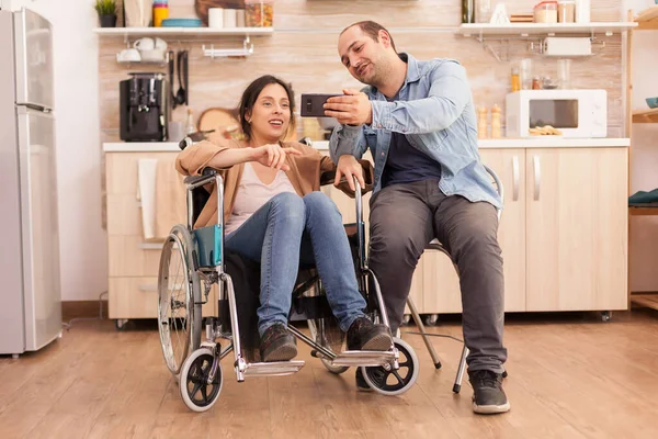 坐在轮椅上的快乐的残疾妇女和丈夫在厨房里自拍 事故后行走残疾的瘫痪残疾妇女融入社会 — 图库照片