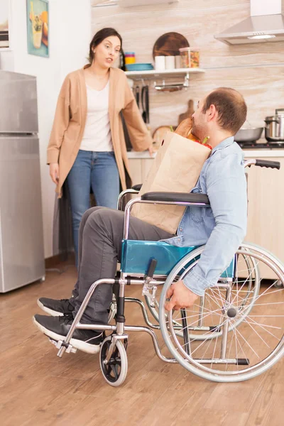 坐在轮椅上的残疾人 带着超市新鲜食品杂货 妻子在厨房里 事故后有行走残疾的瘫痪残疾人融入社会 — 图库照片