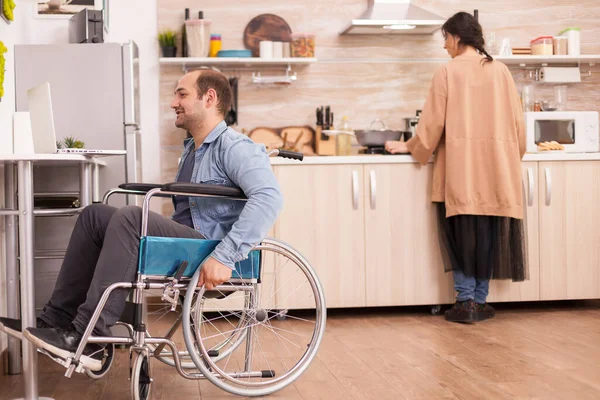 坐在轮椅上的残疾人一边做饭一边打电话到厨房 事故后有行走残疾的瘫痪残疾人融入社会 — 图库照片