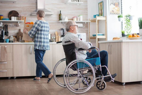 年老体弱的男人微笑着从厨房的窗户往外看 正在打开食品杂货的包装 丧失工作能力 养恤金领取者 残疾人 — 图库照片