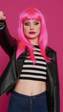 Dikey video: Havalı punk kadın stüdyoda onaylamadığını ve hayal kırıklığına uğradığını gösteriyor. Deri ceketli modaya uygun bir kız kötü sembolden hoşlanmaz, olumsuz bir jest yapar..