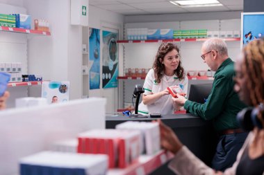 Yaşlı müşteri eczacıyla tartışıyor, tıbbi danışmanlık sırasında hap broşürü istiyor. Eczacı, müşteriye ilaçlarla yardım ediyor. Sağlık hizmetleri desteği