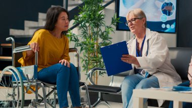 Tekerlekli sandalyedeki Asyalı hastaya danışmanlık yapan yaşlı bir doktor kronik sakatlık ve sakatlık çekiyor. Sağlık sorunu olan bir kadın lobideki doktora muayene oluyor. El kamerasıyla..