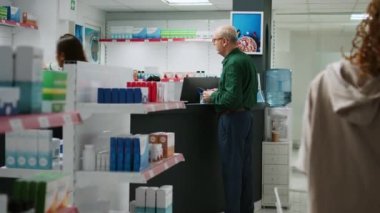 Üst düzey bir müşteri eczaneden reçeteli ilaç almak için cep telefonu ödemesiyle ödeme yapıyor. Eczacıyla ilaç ve vitaminler hakkında konuşan yaşlı kişi.
