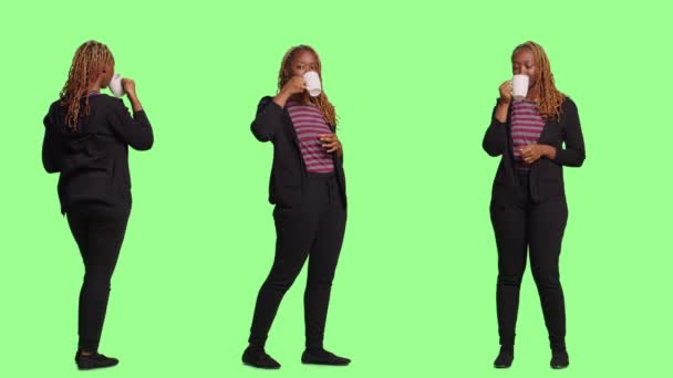 女性模特儿在绿屏的背景下喝着杯子里的咖啡 全身站在绿屏的背景下 享受咖啡因饮料和点心 感到快乐 — 图库视频影像