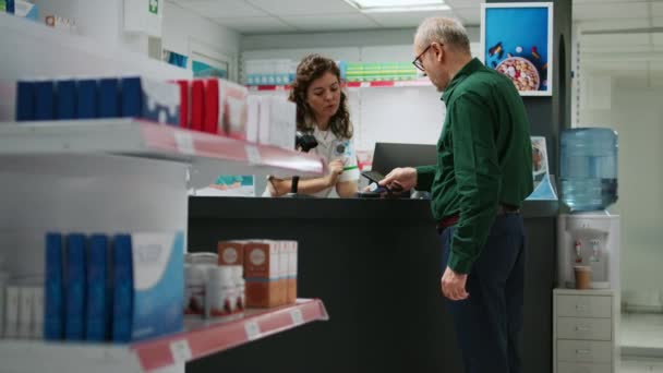 老年顾客在药店柜台购买处方药药丸 用手机付款 老年人与药剂师谈论药物和维生素 — 图库视频影像